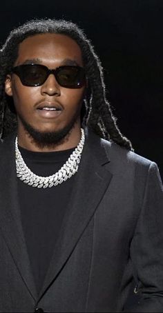 a man with dreadlocks wearing sunglasses and a black suit on the runway at a fashion show