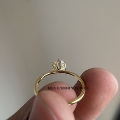 a hand holding a gold ring with a flower on the top and bottom, in front of a white wall