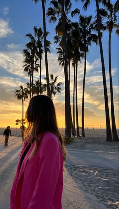 a woman standing in front of palm trees on the beach at sunset with people walking by