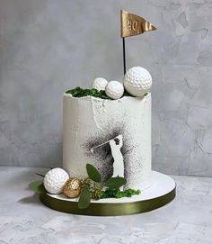 a white cake decorated with golf balls and a gold flag on top is sitting on a table