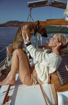 a woman sitting on the back of a boat holding a dog