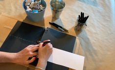 a person writing on a piece of paper next to some pens and pencils in a container