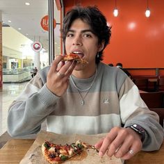 a man sitting at a table with a slice of pizza in front of his mouth