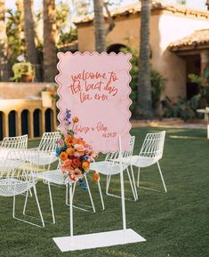 a welcome sign is set up in the grass with white chairs and flowers on it