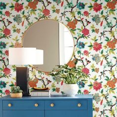 a blue dresser sitting next to a mirror on top of a wooden table in front of a wallpapered wall