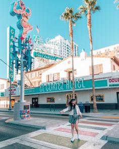 a woman crossing the street in front of a building with neon signs and palm trees