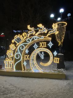 a lighted clock in the snow with lights on it's face and numbers displayed