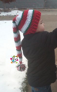 a young boy wearing a red, white and green hat while standing in the snow