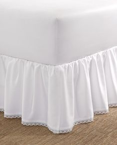 a white bed skirt with ruffles on the bottom and bottom, in front of a carpeted floor