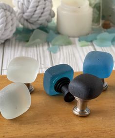 three different colored glass knobs sitting on top of a wooden table next to candles