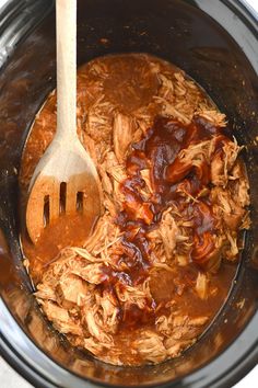 the meat is being cooked in the slow cooker with a wooden spoon and fork