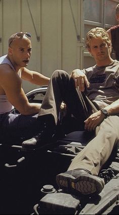 two men sitting on the hood of a car