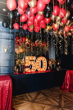 balloons and streamers fill the ceiling at a 50th birthday party with red, black, and gold decorations