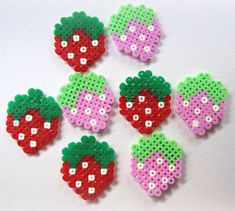 six perler bead strawberrys on a white surface with green, red and pink beads