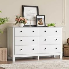 a white dresser with flowers and pictures on top