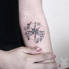 a woman's arm with a compass and flowers tattoo on the left inner arm