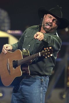 a man wearing a cowboy hat and holding a guitar in his right hand while singing into a microphone