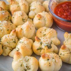 small rolls with cheese and herbs on a plate next to a bowl of tomato sauce