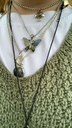 a close up of a person wearing a sweater and some necklaces on their neck