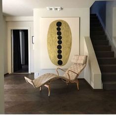 a chair and ottoman in front of a painting on the wall next to a stair case