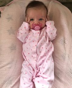 a baby laying on top of a bed with its head in her hands and wearing a pacifier