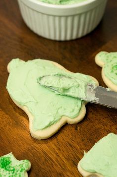 green frosted cookies being cut into shapes with a knife on the table next to them