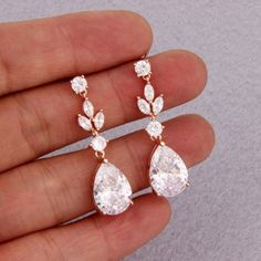 a hand holding two pairs of earrings with white stones on each earring and the other one has a tear shaped diamond