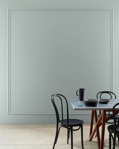 two chairs and a table with plates on it in front of a wall that is painted gray