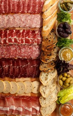 an assortment of meats, bread and olives on a cutting board with other foods