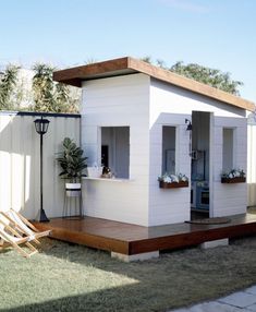 a small white house sitting on top of a grass covered field next to a wooden deck