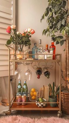 a bar cart filled with bottles and glasses on top of a table next to a potted plant