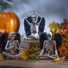 three skeleton figurines sitting on top of a wooden table next to pumpkins