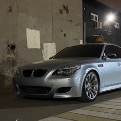 a silver car parked in front of a building at night with its lights turned on