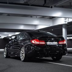 a black car parked in an empty parking garage with its lights on and it's rear end showing