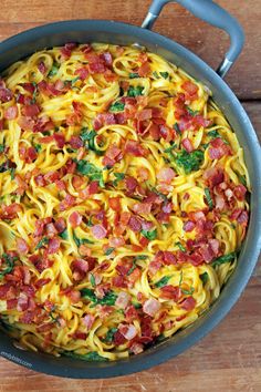 a pan filled with pasta and bacon on top of a wooden table