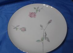 a white plate with pink flowers on it sitting on a blue cloth covered tablecloth