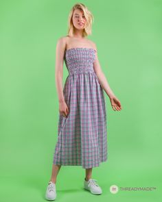 a woman standing in front of a green background wearing a purple and white checkered dress