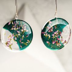 two glass earrings with flowers on them hanging from metal earwires against a white background