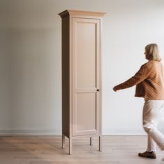 a woman standing next to a tall wooden cabinet in an empty room with hard wood flooring