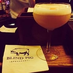 a glass of beer sitting on top of a wooden table next to a paper napkin