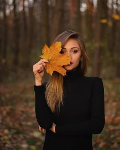 a beautiful young woman holding an autumn leaf in front of her face and looking at the camera