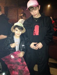 two young men standing next to each other in front of a brick wall and poster