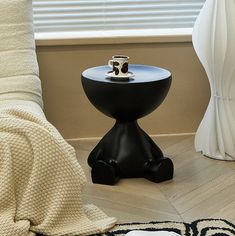 a black table sitting on top of a wooden floor next to a white chair and window