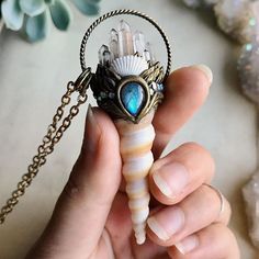 a person holding a small shell with a blue stone in it's center on a chain