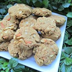 a white plate topped with cookies on top of green leaves covered ground next to bushes