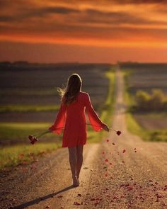 a woman in a red dress is walking down the road with petals on her hands