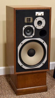 a speaker sitting on top of a wooden stand next to a carpeted floor and wall