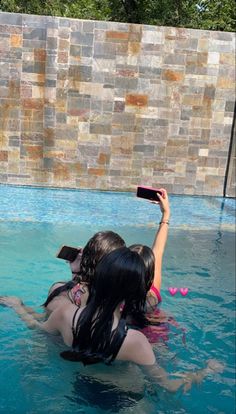 two women in the pool taking pictures with their cell phones while one holds up her phone