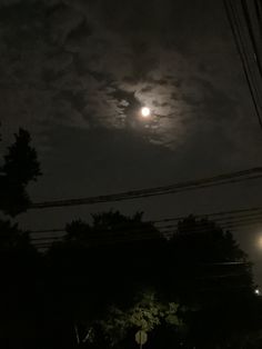 the full moon shines brightly in the night sky above some trees and power lines