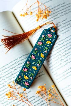 an open book with flowers on it next to a tasseled bookmark and dried flowers